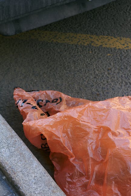A black outdoor waste bin with the label 'ST. JOHN'S' positioned on a sidewalk beside a curb at night. The bin is filled with various discarded items, including cardboard, paper, and plastic. The city